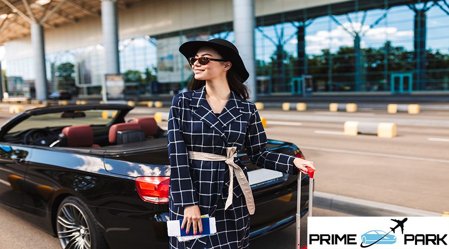 Beautiful smiling girl in sunglasses and black hat holding passport with flight ticket joyfully looking aside near airport with cabriolet car on background