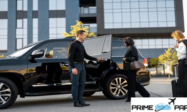 Chauffeur helps business couple to get in the car, opening a door of a luxury black taxi. Man and woman having a business trip together