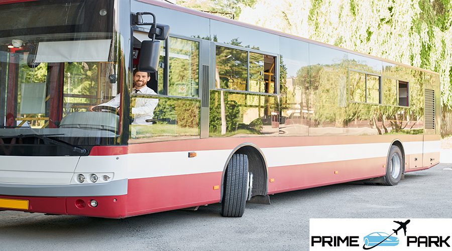 Elegant driver sitting in shuttle bus, smiling to camera at summer day. Front view of happy man sitting on driver's seat, working, going on route way in city. Concept of transportation, work, traffic.