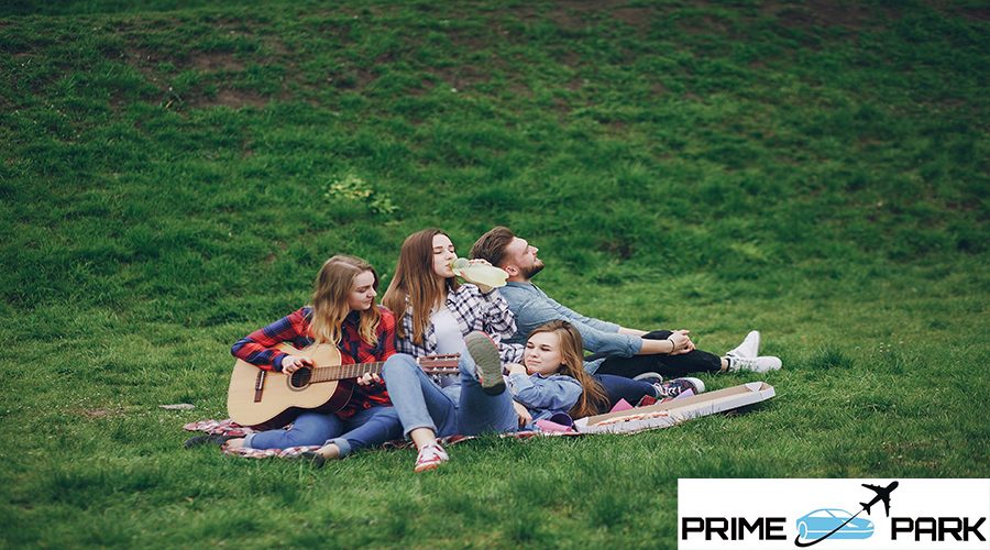 Three beautiful girls with handsome boy sitting in a park on a blanket with guitar