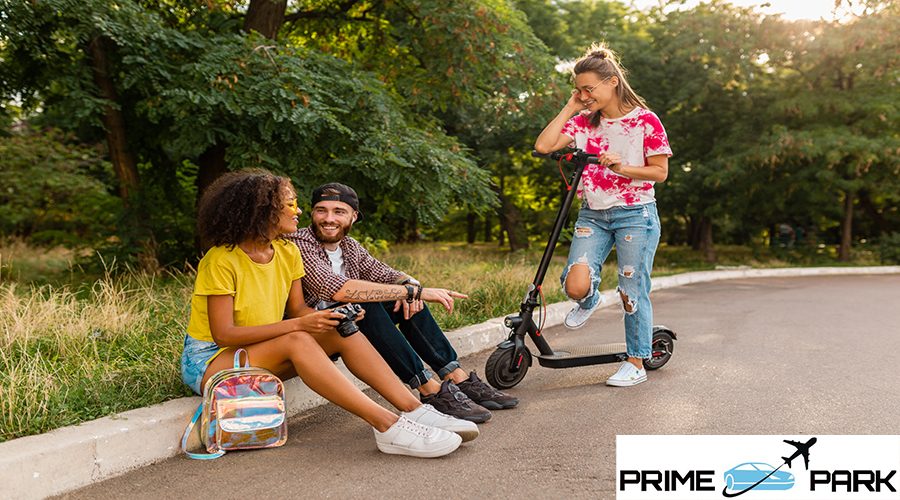 happy young company of talking smiling friends sitting in park, man and women having fun spending time together, colorful summer hipster fashion style, riding on electric scooter, modern youth