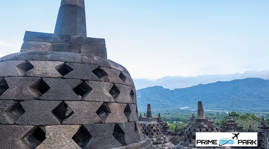 A detailed close-up of the stone carvings and stupas at the Borobudur Temple, showcasing the intricate craftsmanship and historical significance against a natural landscape.