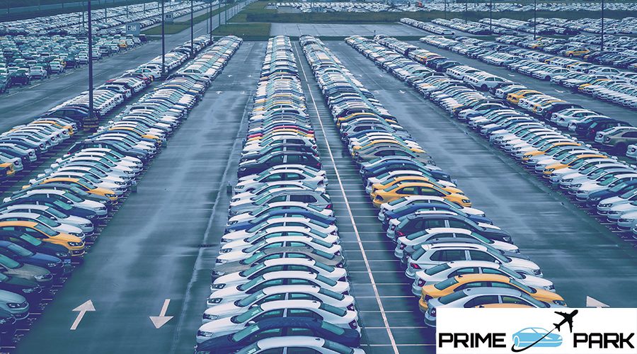 New cars parked in a distribution center on a cloudy day and car factory buildings with pipes. Parking in the open air.