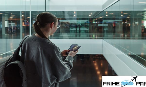Young woman with a backpack holding a passport and smartphone while looking through glass at a contemporary airport. Concept of international travel, identity verification and global mobility